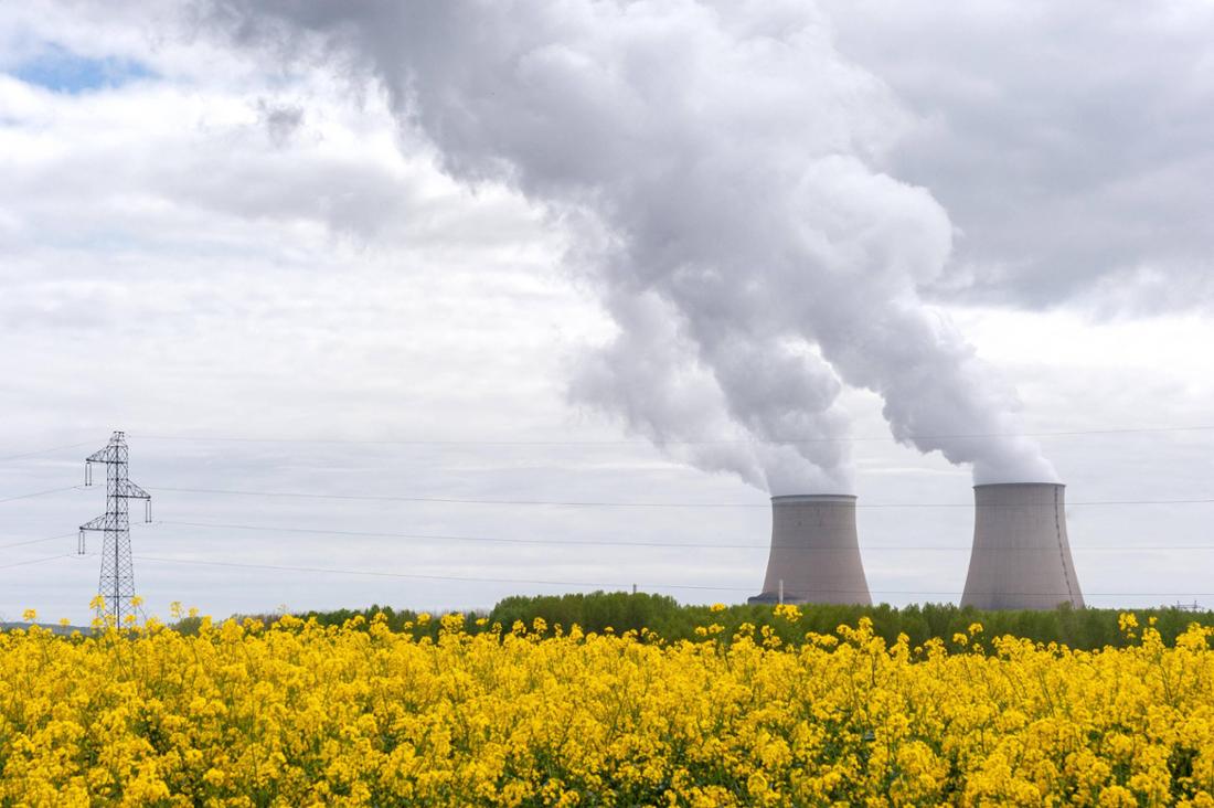 Die Kühltürme des Atomkraftwerks Nogent-sur-Seine ragen hinter Feldern hervor. Auf der linken Seite ist der Turm einer Hochspannungsleitung.