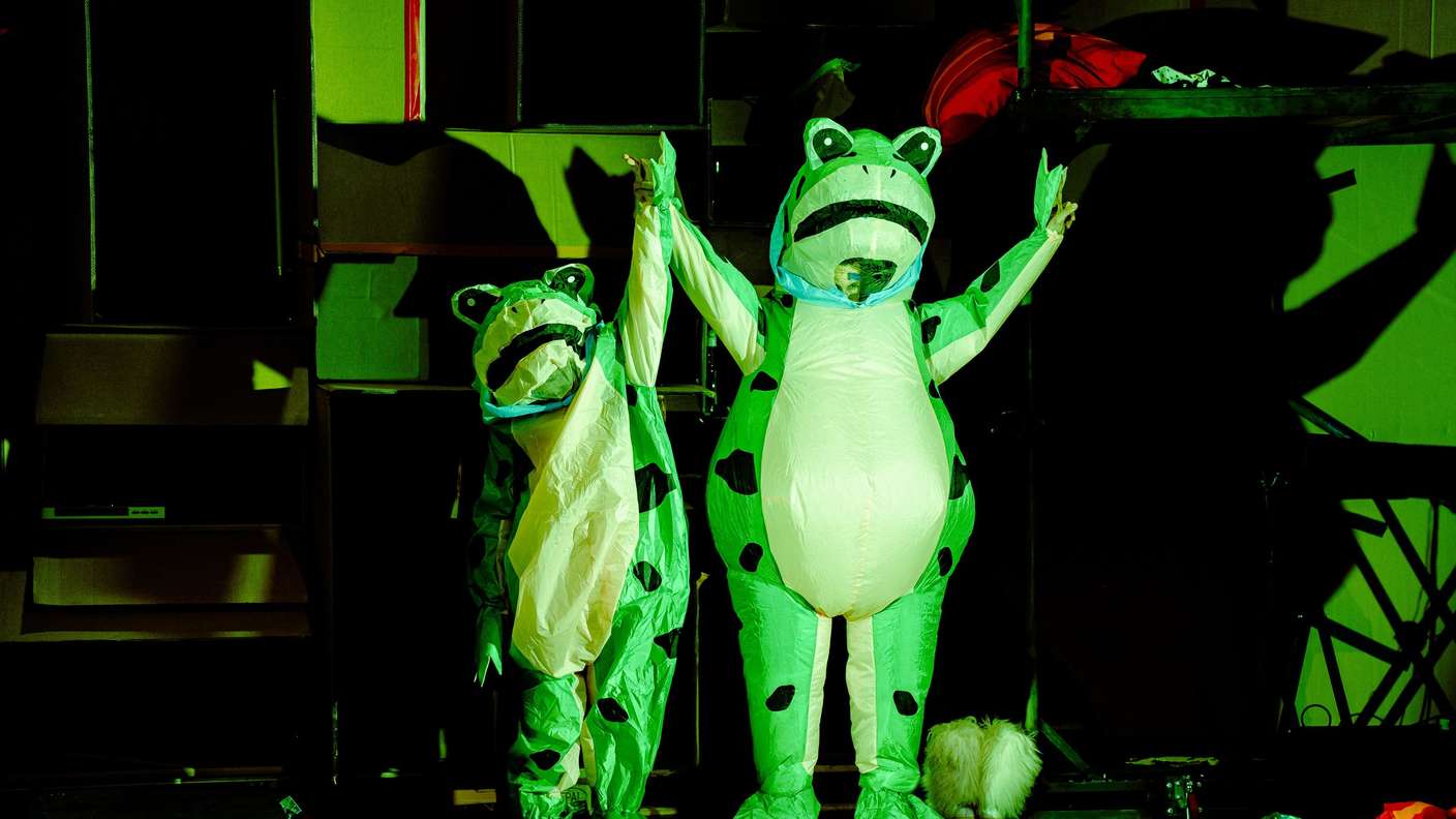 Zwei Schauspieler im aufblasbaren Froschkostüm, die Quilters, heben die Arme und  rufen zum Protest auf. 