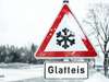 Ein Verkehrsschild warnt vor Glatteis auf schneebedeckter Straße.