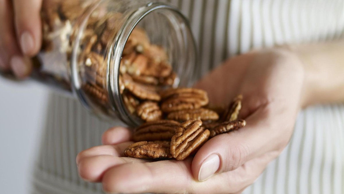 Unter den pflanzlichen Lebensmitteln sind Pekannüsse eine der besten Zinkquellen. Eine Frau entnimmt Pekannüsse aus einem Glasgefäß
