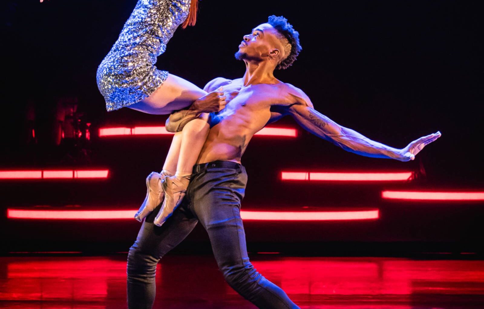 Zu sehen ist eine Tänzerin im Glitzerkleid und ein Tänzer mit freiem Oberkörper auf der Bühne.