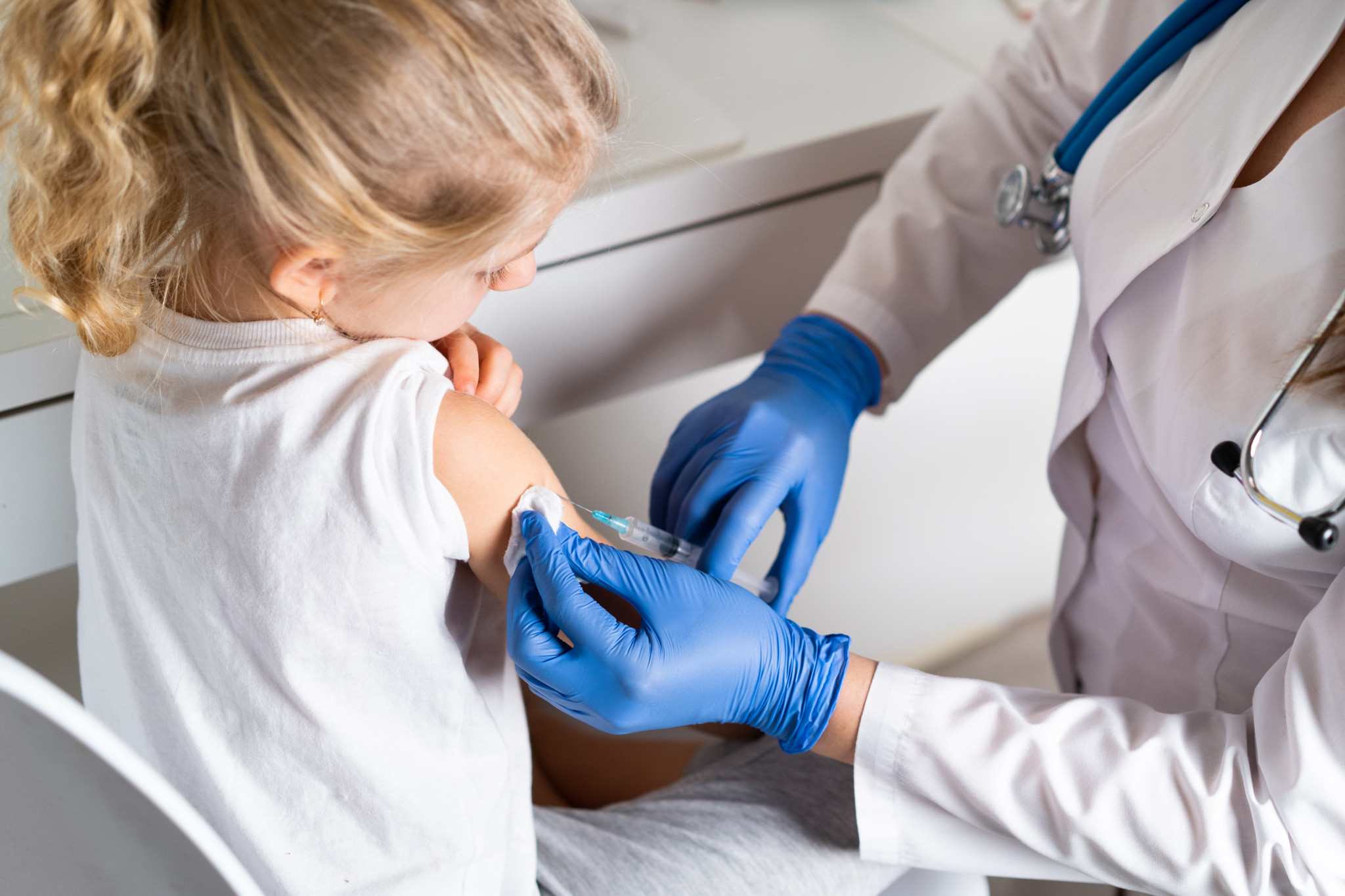 Eine Ärztin impft ein kleines Mädchen am Arm in einer Praxis.