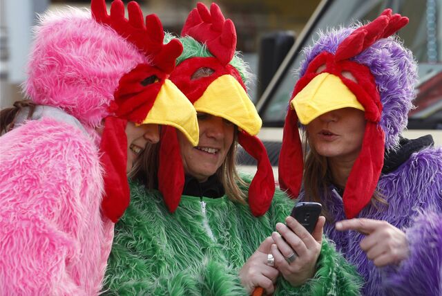 Verkleidete Jecken schauen in Düsseldorf (NRW) beim Start des Straßenkarnevals auf ein Smartphone.