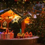 Geschmückte Weihnachtsbäume und beleuchtete Buden und Geschenke bei Schnee auf einem Weihnachtsmarkt.