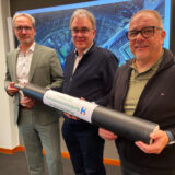 Drei Männer stehen zusammen und halten ein Stück Fernwärme-Leitung.