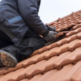 Ein Dachdecker mit Ziegeln in der Hand arbeitet auf einem Dach