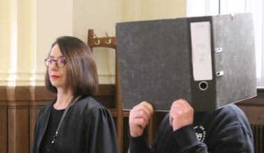 Angeklagter steht hinter Ordner im Gericht neben seiner Anwältin.