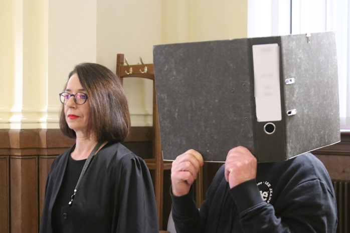 Angeklagter steht hinter Ordner im Gericht neben seiner Anwältin.