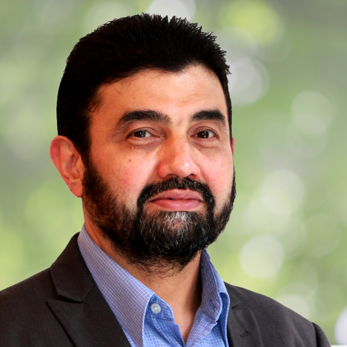 Porträt eines Mannes mit Bart in einem Anzug vor unscharfem grünem Hintergrund.