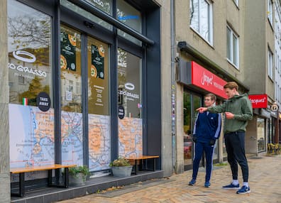 Laufguide Mathis Brandt (23, rechts) von Running City Tours ist unterwegs mit KN-Reporter Moritz Krüger joggend die Stadt zu entdecken. Auf der Tour gibt es auch immer wieder Tipps, wo es sich lohnt mal Halt zu machen, wie hier beim Zio Grasso in der Holtenauer Straße mit einer neapolitanishcen Pizza zum Mitnehmen.