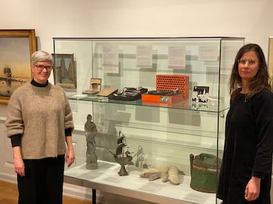 Vom Gemälde mit Kiel-Bezug über silberne Löffel bis zum historischen Schallplattenspieler der weltweit bedeutenden Kieler Firma Elac: Museumsleiterin Sonja Kinzler (re.) und Kuratorin Katrin Seiler-Kroll vor einer Vitrine, die das Spektrum der Sammlung im Depot zeigt.