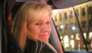 Blondhaarige Frau hat den Kopf nach rechts gedreht und schaut zur Kamera.