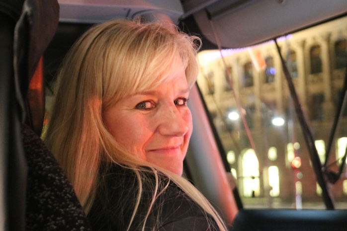 Blondhaarige Frau hat den Kopf nach rechts gedreht und schaut zur Kamera.