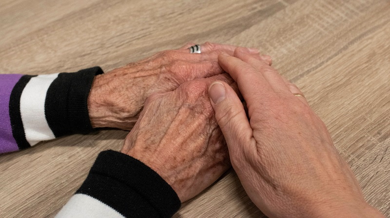 Bildbeschreibung: Jemand der von einer älteren Frau die Hand hält.