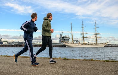 Laufguide Mathis Brandt (23, rechts) von Running City Tours ist unterwegs mit KN-Reporter Moritz Krüger joggend die Stadt zu entdecken. An der Kiellinie gehts vorbei an der Gorch Fock, nicht ohne Wissenswertes zum Kieler Schiff.