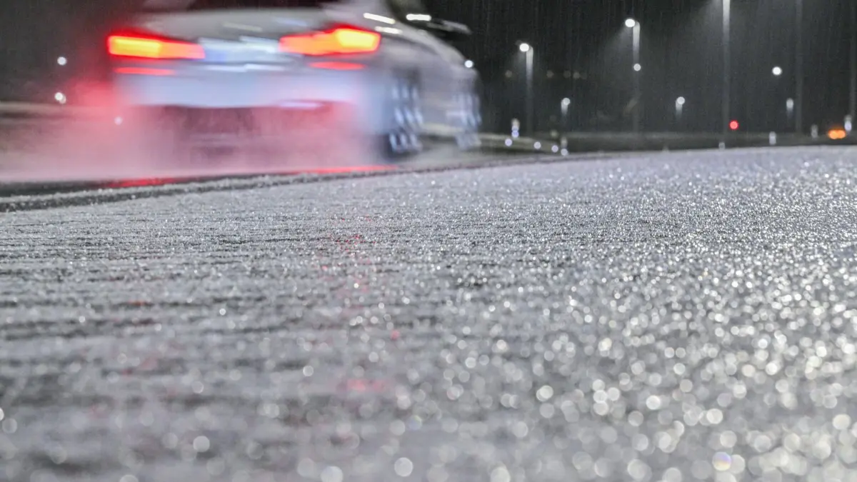 Wetter in Bayern: 24.11.2025, Bayern, München: Ein Auto fährt in der Nähe des Flughafens München an Eis auf einer Straße vorbei. Foto: Jason Tschepljakow/dpa +++ dpa-Bildfunk +++