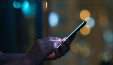 Eine Person schaut im Dunkeln auf ein leuchtendeds SMartphone und tippt SMS oder Whatsapp