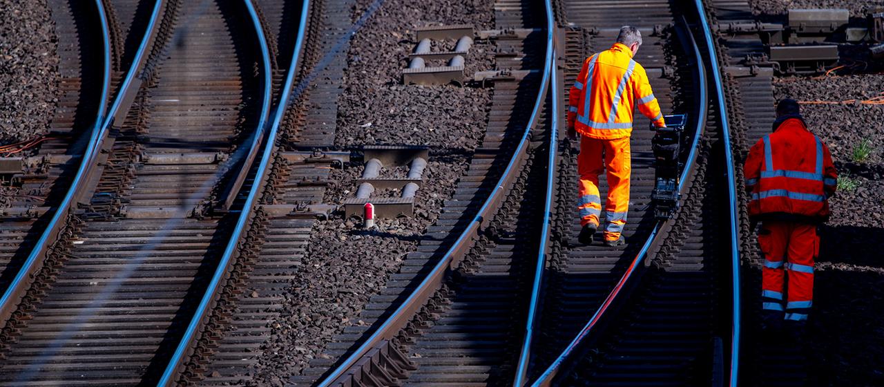 Zwei Bauarbeiter gehen im Gleisbett neben den Bahnschienen
