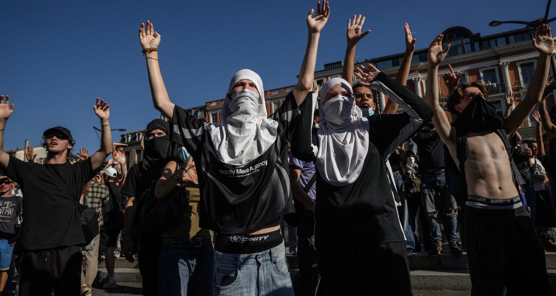 Teilweise vermummte Personen stehen auf einer Demonstration und heben ihre Hände in die Luft