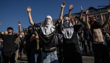 Teilweise vermummte Personen stehen auf einer Demonstration und heben ihre Hände in die Luft