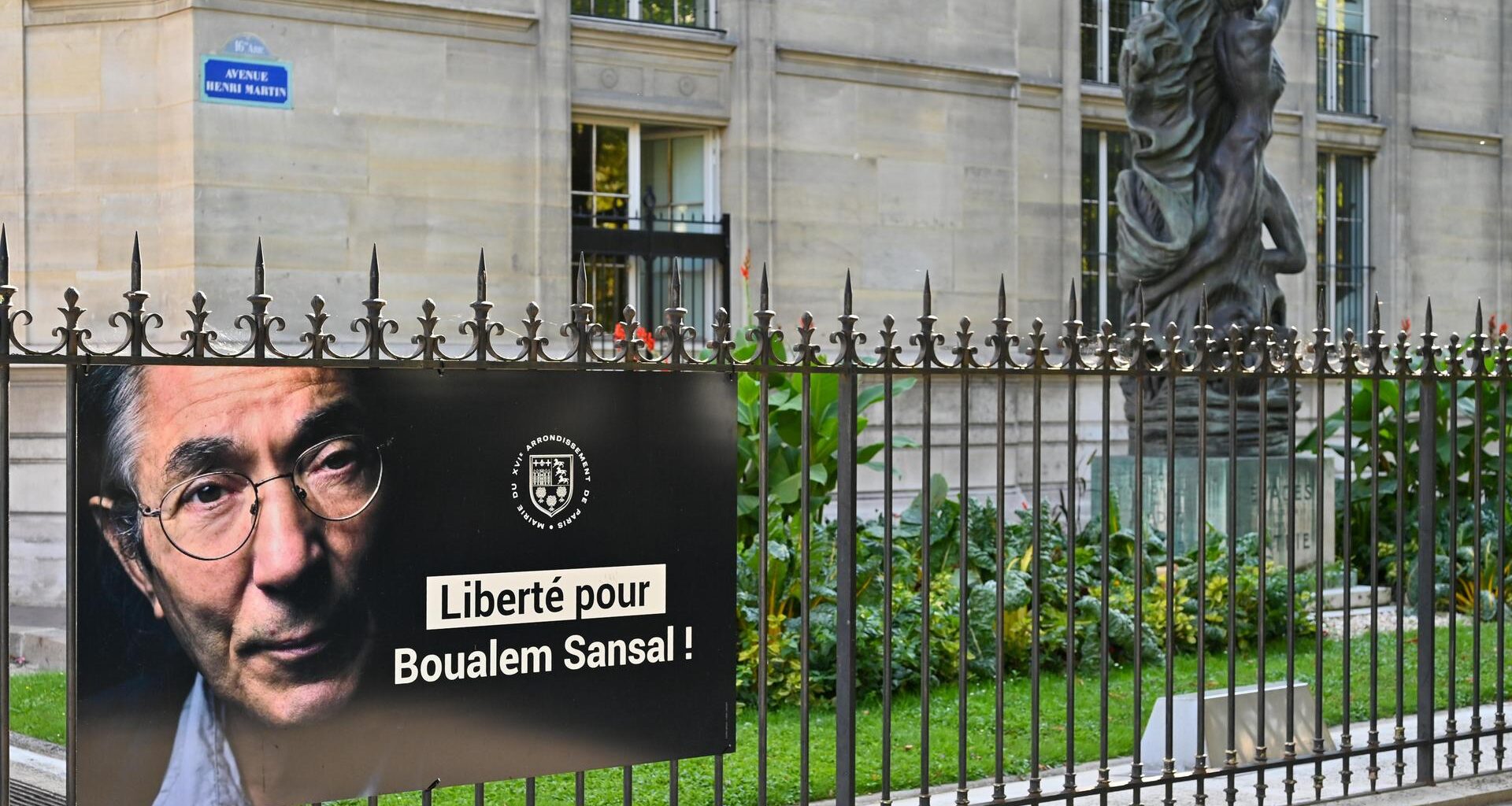 Ein Poster mit einem Porträt von Boualem Sansal und den Worten "Liberté pour Boualem Sansal!" hängt an einem Zaun im 5. Arrondissement in Paris.