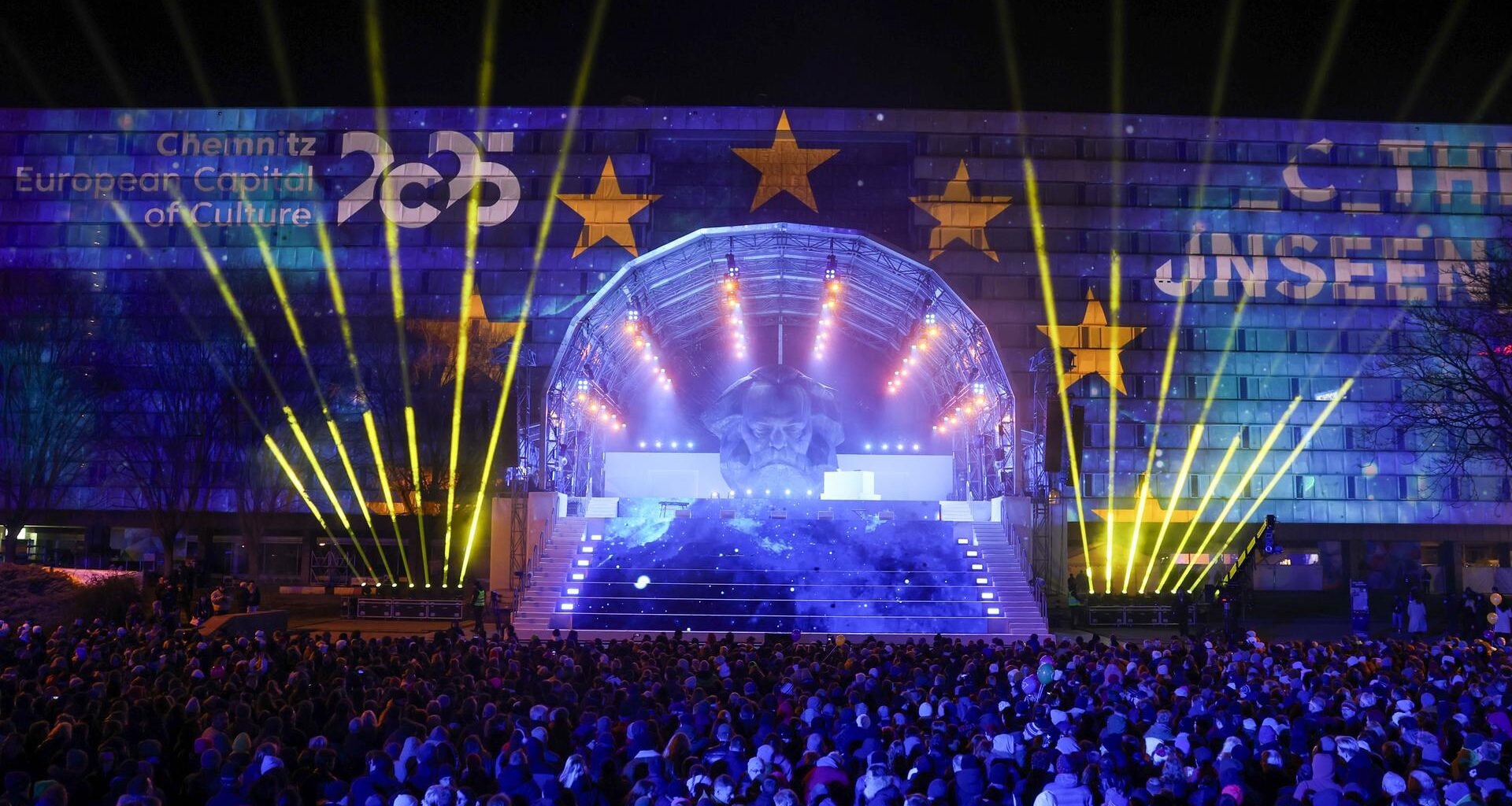 Eine Bühne mit einer Laser-Show in Chemnitz. Davor stehen viele Menschen. Im Hintergrund ist eine riesige Büste von Karl Marx zu sehen.