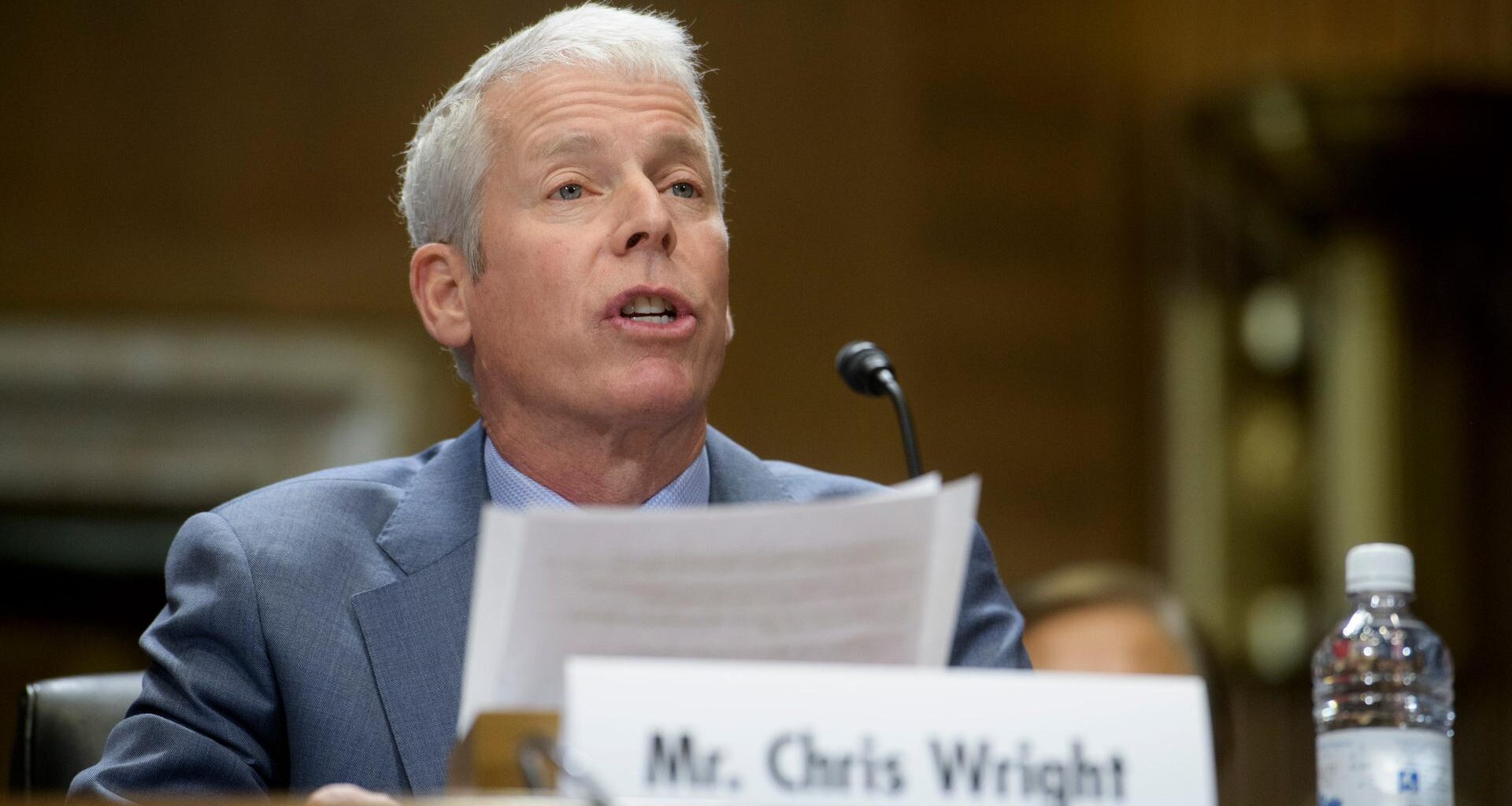 Chris Wright sitzt bei einer Veranstaltung hinter einem Mikrofon. Vor ihm steht sein Namensschild.