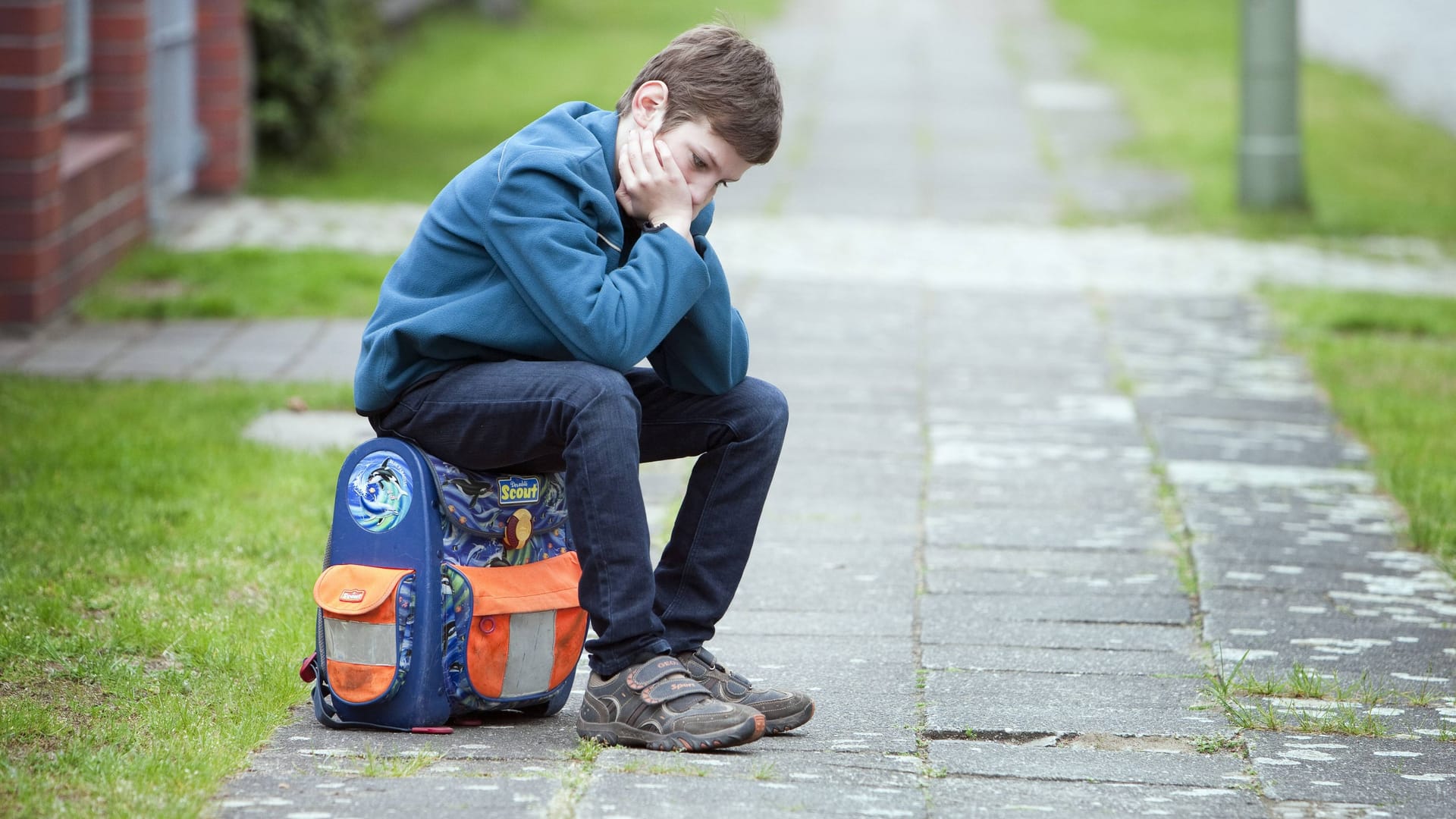 Ein trauriges Kind sitzt auf seinem Schulranzen (Symbolbild): Viele Kinder im Hamburger Süden wachsen mit wenig Geld auf.