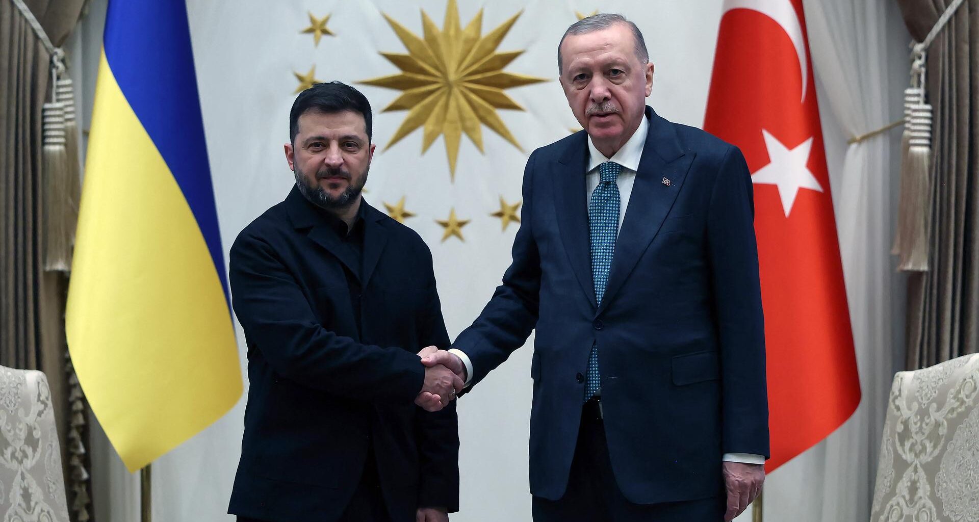 Der türkische Präsident Erdogan und sein ukrainischer Amtskollegen Selenskyj reichen sich die Hand. Hinter ihnen stehen die Flaggen ihrer Länder.