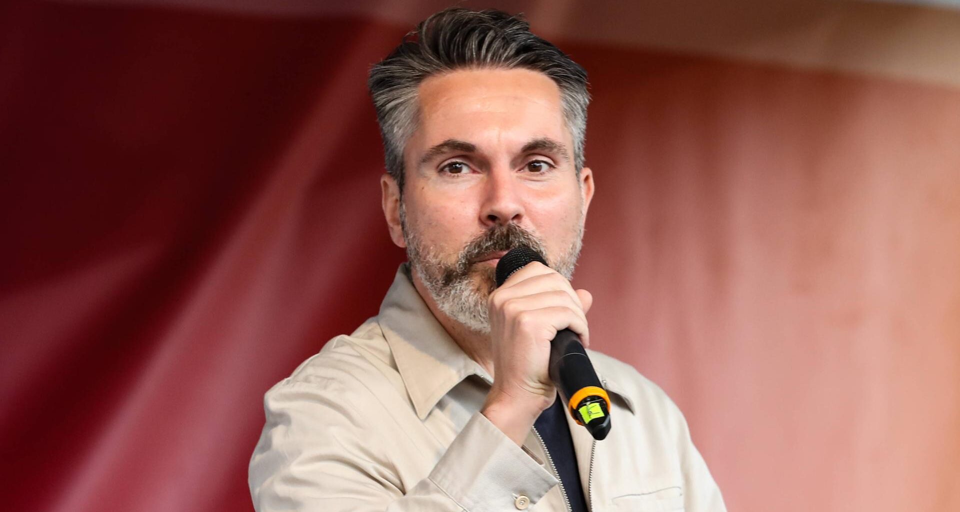 Fabio De Masi spricht in ein Handmikrofon. Im Hintergrund: ein rotes Transparent