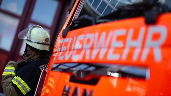 Eine Einsatzkraft der Feuerwehr steht neben einem Einsatzfahrzeug der Feuerwehr.