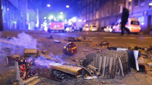 Abgebrannte Böller liegen nach der Silvesternacht auf der Straße im Hintergrund sind Feurwehrfahrzeuge zu sehen.