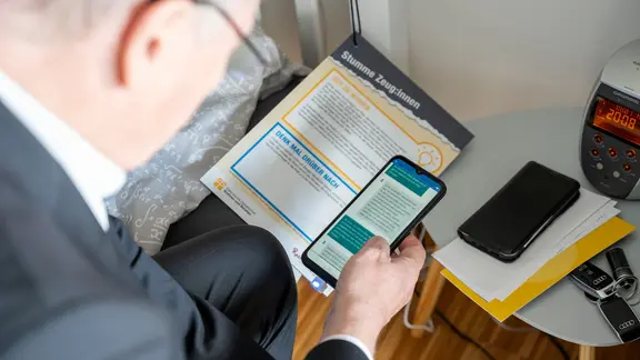 Ein Mann schaut mit seinem Handy ein Ausstellungsstück an. | Diakonische Gesellschaft Wohnen und Beraten, Torge Bleicher Ein Mann schaut mit seinem Handy ein Ausstellungsstück an.