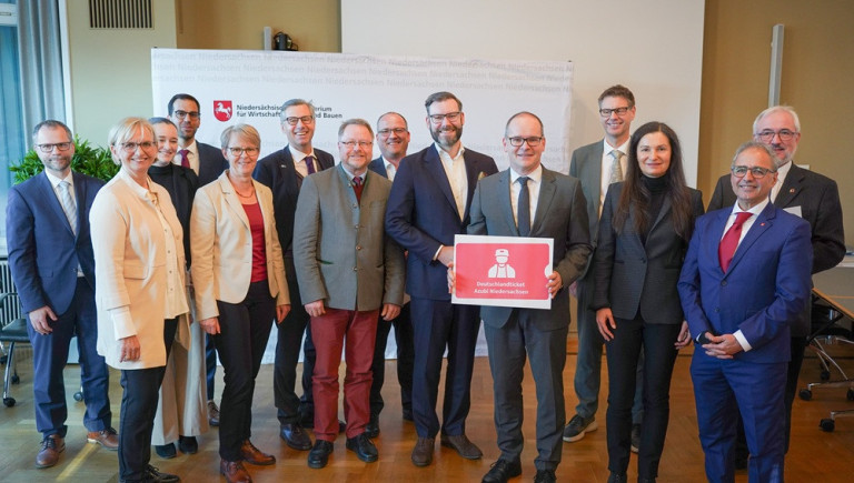 Gruppenbild beim Niedersächsischen Ministerium für Wirtschaft, Verkehr, Bauen und Digitalisierung mit Schild 'Deutschlandticket Azubi Niedersachsen'