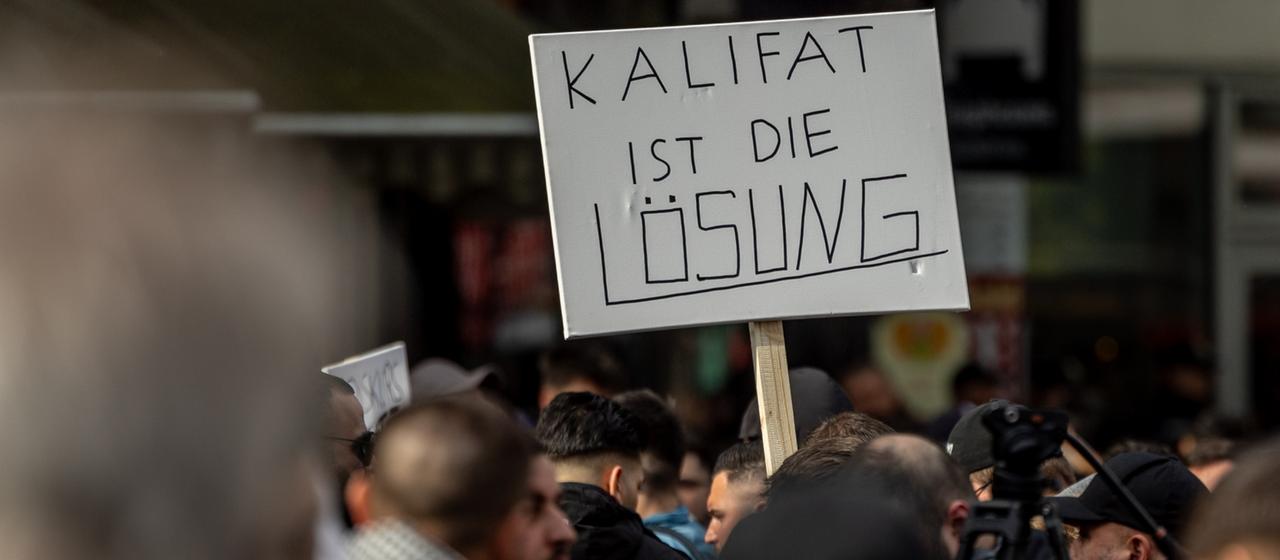 Teilnehmer einer Islamisten-Demonstration in Hamburg halten ein Plakat mit der Aufschrift "Kalifat ist die Lösung" in die Höhe. | dpa Teilnehmer einer Islamisten-Demonstration in Hamburg halten ein Plakat mit der Aufschrift "Kalifat ist die Lösung" in die Höhe.