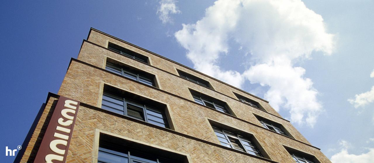 Foto eines Gebäudes aus der Froschperspektive, an der Gebäudeecke ein Schild "Mouson".