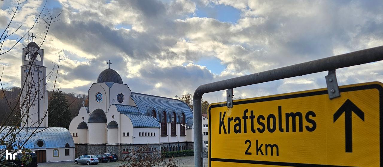 Ein Ortsschild mit der Aufschrift Waldsolms, im Hintergrund ein Kloster