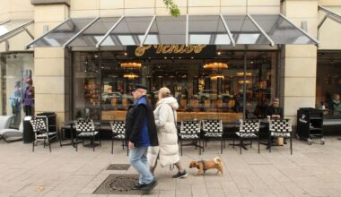 Tchibo-Filiale bei Tageslicht, zwei Spaziergänger laufen daran vorbei.