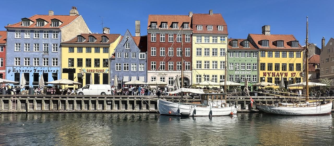 Menschen spazieren vor bunten Häusern am Wasser entlang in Kopenhagen