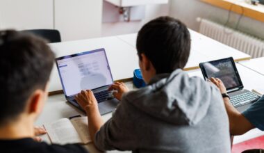 Drei Schüler von hinten an einer Schulbank; zwei von ihnen schauen in ein Tablet.