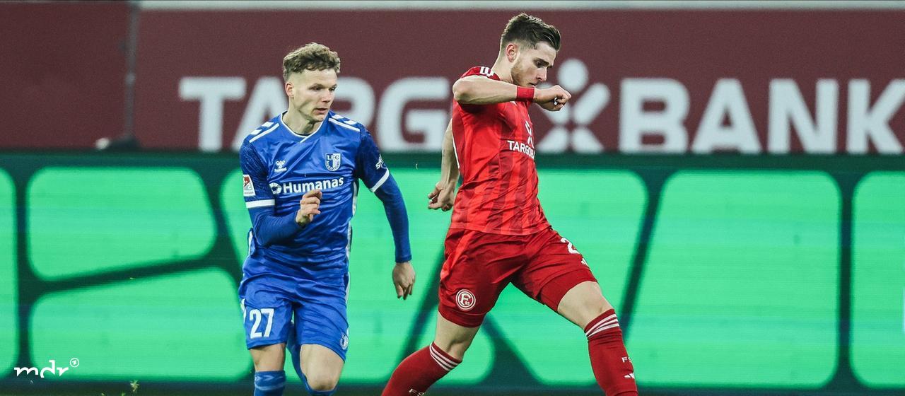 In einem Fußballspiel läuft Philipp Hercher (1.FC Magdeburg, 27) Tim Rossmann (Fortuna Düsseldorf, 21) und dem Ball hinterher.