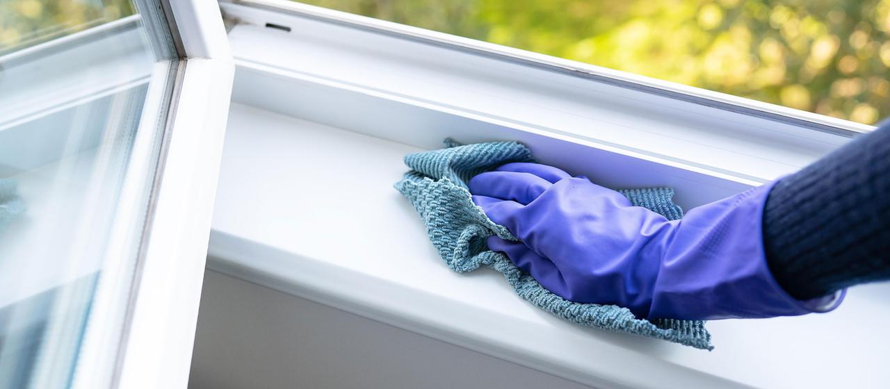Eine Frau wischt mit einem Tuch ein Fensterbrett