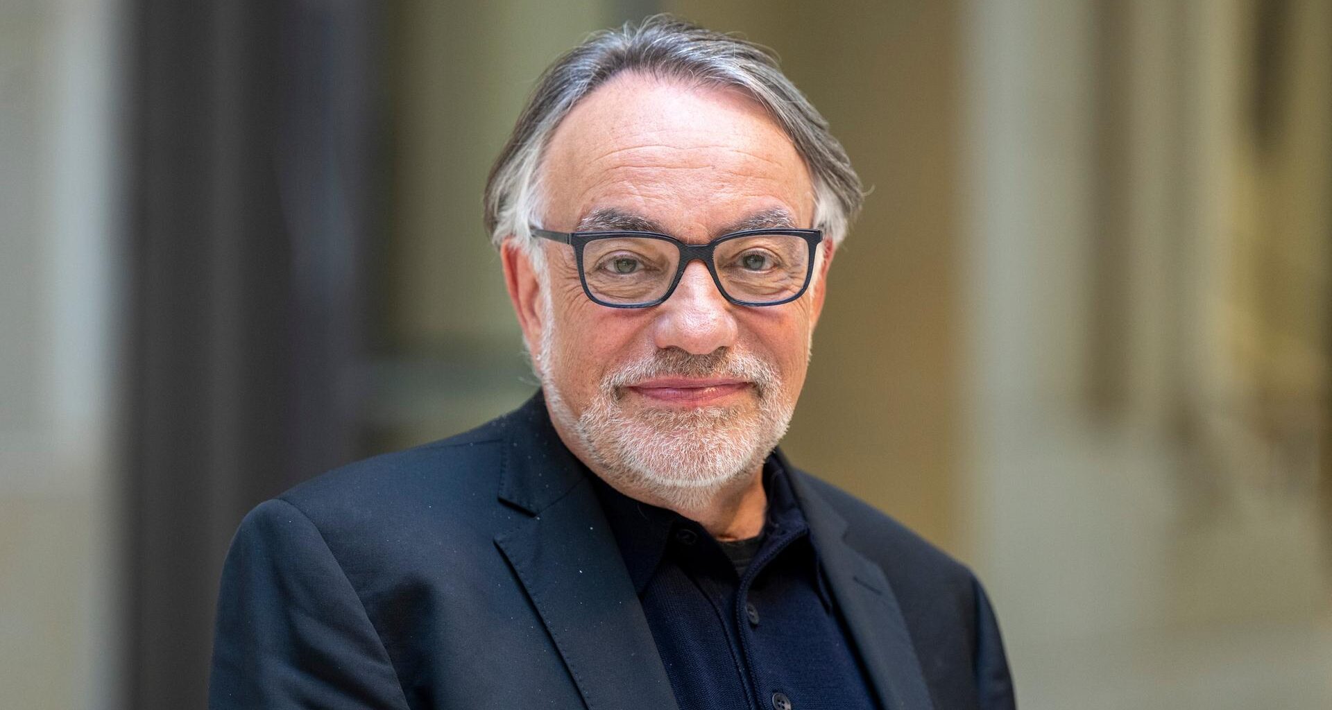 Natan Sznaider im Vorfeld einer Veranstaltung. Er lächelt zurückhaltend, der Hintergrund ist unscharf. Er trägt eine Brille mit dunklem Rand und ein dunkelblaues Sakko.