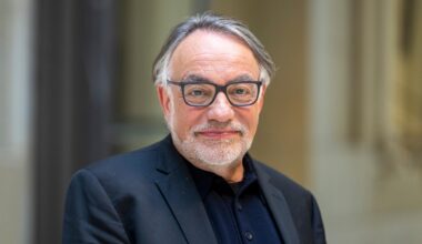 Natan Sznaider im Vorfeld einer Veranstaltung. Er lächelt zurückhaltend, der Hintergrund ist unscharf. Er trägt eine Brille mit dunklem Rand und ein dunkelblaues Sakko.