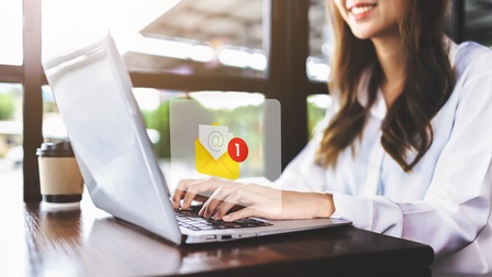 Eine junge Frau vor ihrem Laptop - darüber ein E-Mail-Zeichen