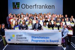 Vertreterinnen und Vertreter der oberfränkischen Startchancen-Schulen mit Kultusministerin Anna Stolz (vorne, 3. v.l.), die die Teilnahmeplaketten im Rahmen der Auftaktveranstaltung in Fürth überreichte./Foto: Daniel Karmann stmuk