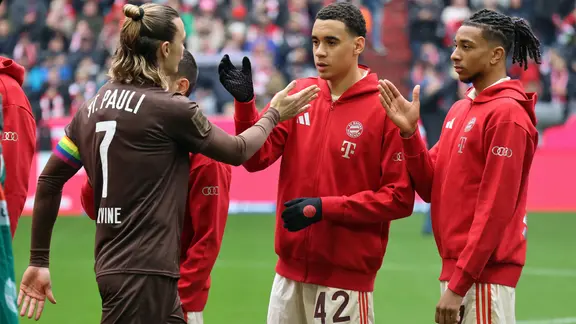 Jackson Irvine (l.) klatscht mit den Münchnern Jamal Musiala (M.) und Raphael Guerreiro ab. | picture alliance / Lackovic | Mladen Lackovic Jackson Irvine (l.) klatscht mit den Münchnern Jamal Musiala (M.) und Raphael Guerreiro ab.