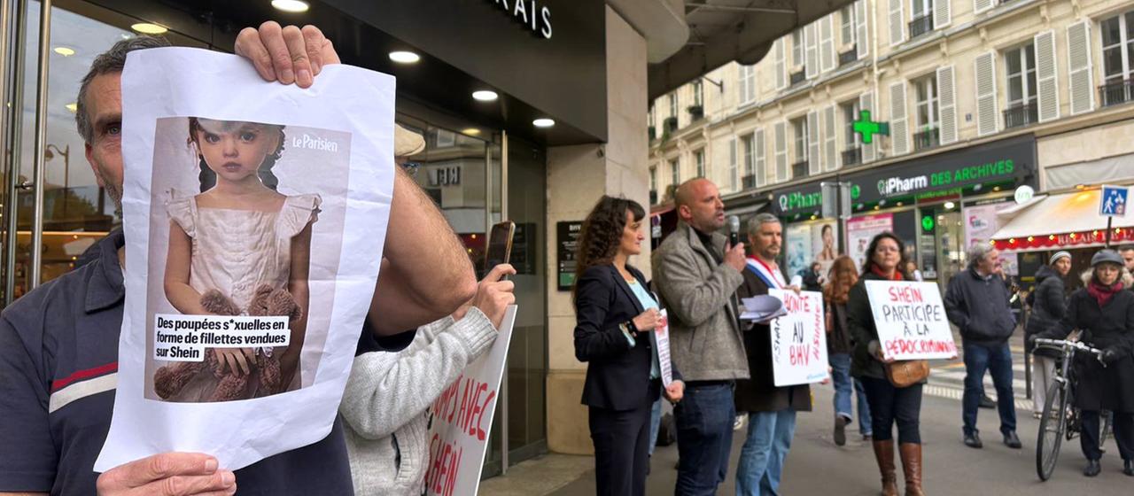 Ein Demonstrant hält ein Bild einer kindlichen Sexpuppe vor dem Kaufhaus BHV Marais in Paris. | AP Ein Demonstrant hält ein Bild einer kindlichen Sexpuppe vor dem Kaufhaus BHV Marais in Paris.