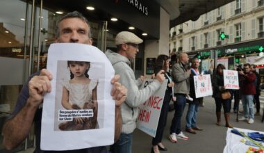 Mehrere Menschen stehen vor dem Eingang eines kaufhauses und halten beschriftete Protestschilder sowie vergrößerte Fotos der Sexpuppen.