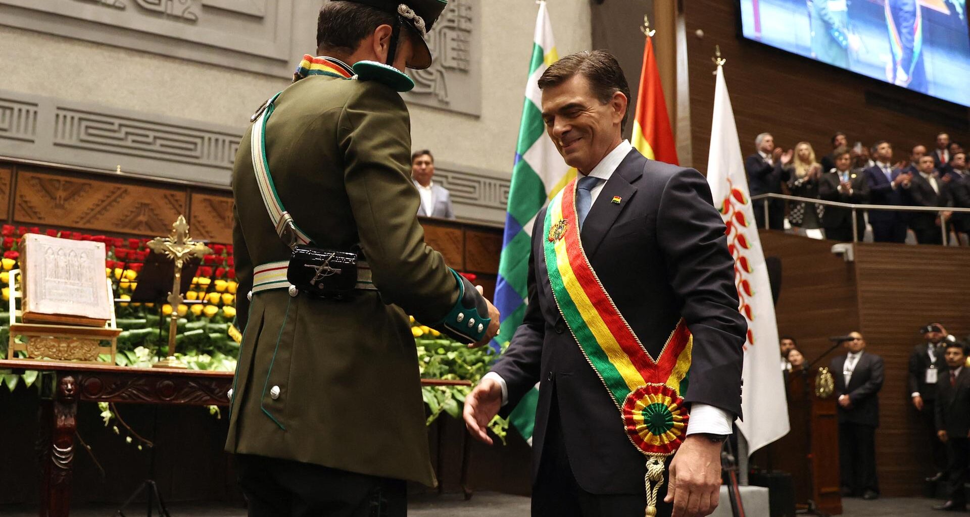 Der lächelnde Paz trägt die Schärpe, die er von einem Armeeangehörigen in Paradeuniform überreicht bekommen hat. Dahinter eine vollbesetzte Tribüne.